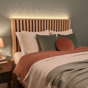 Vue principale de la tête de lit tasseaux verticaux TSX en épicéa et chêne massif avec lumière LED au-dessus, ambiance chambre chaleureuse.