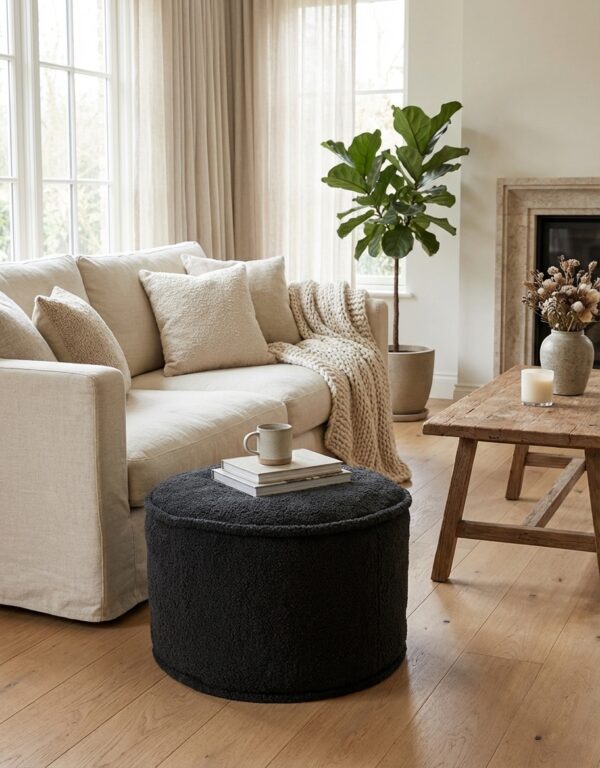 Pouf en tissu gris placé dans un salon moderne, avec une tasse et un livre posés dessus. Référence produit D0117-A.