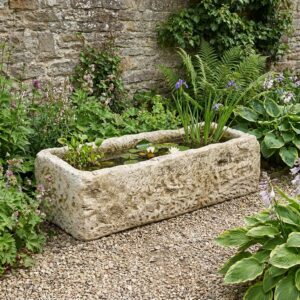 Image principale de l'abreuvoir en pierre ancien, référence 280038, utilisé comme bac à fleurs dans un jardin