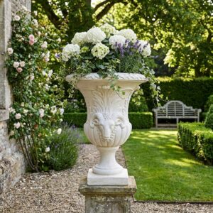 Vase Médicis 70cm avec tête de bélier en pierre, référence 213156, disposé dans un jardin verdoyant